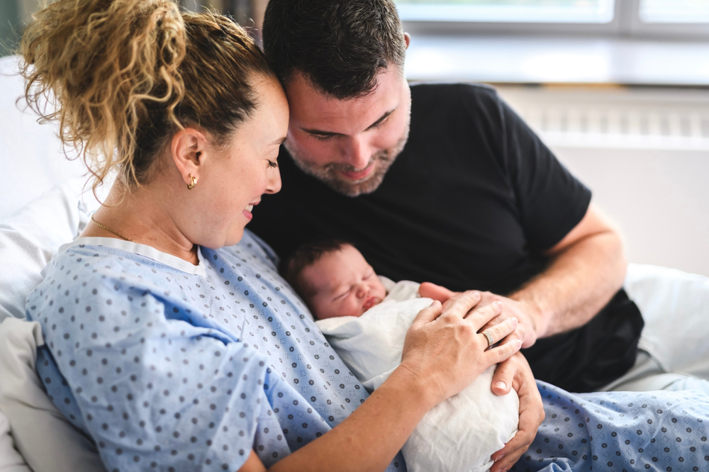 Parents holding their newborn baby in a hospital bed.