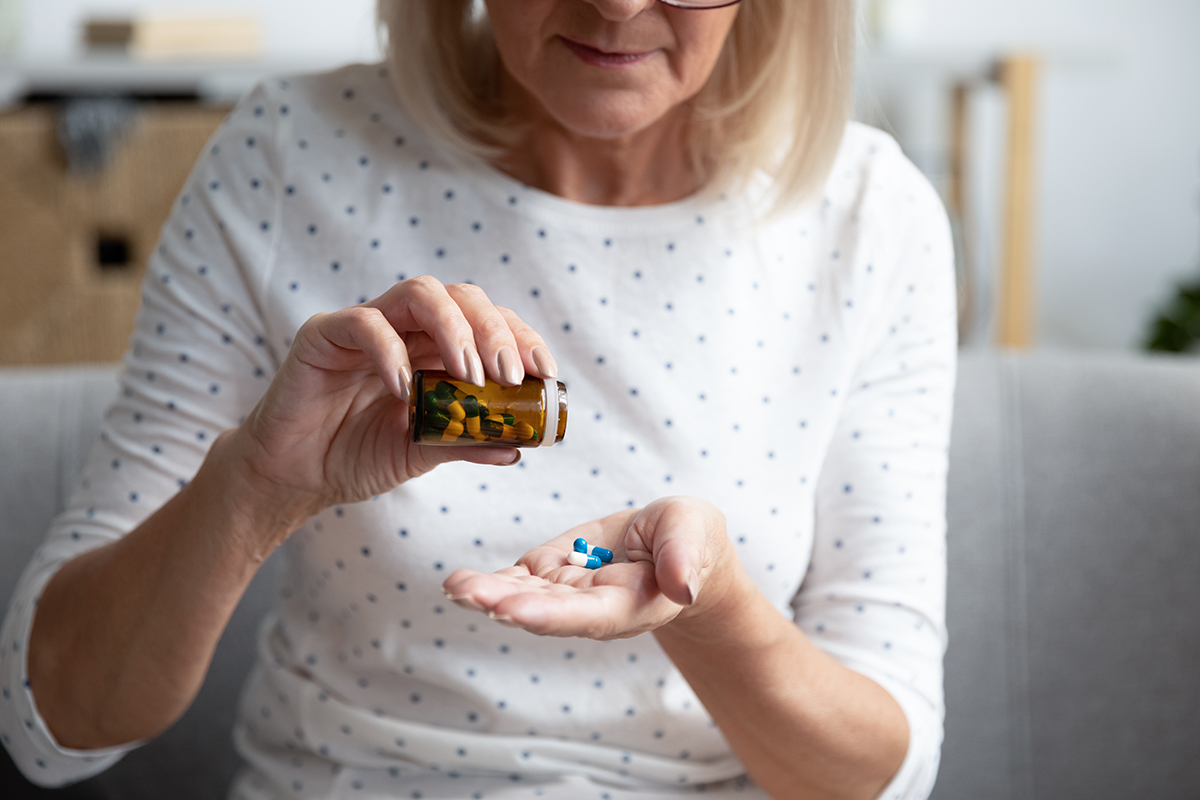 An older adult pouring medicine out of a bottle into her hands.